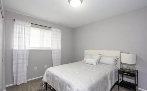 A bedroom with a white bed and a window with curtains.