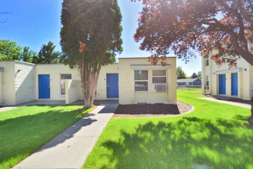 a white building with blue doors and a lawn and trees