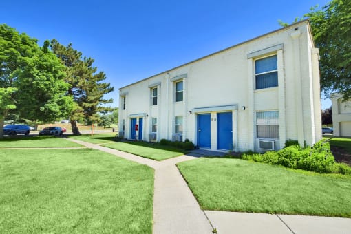 the exterior of a white building with blue doors and a sidewalk