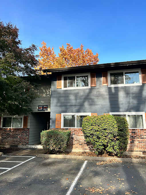 A grey building with a parking lot in front.
