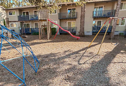 A playground with a blue swing set and a red slide in front of apartment buildings.