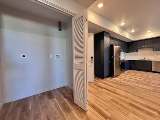 A kitchen with a refrigerator and cabinets in a room with wooden flooring.