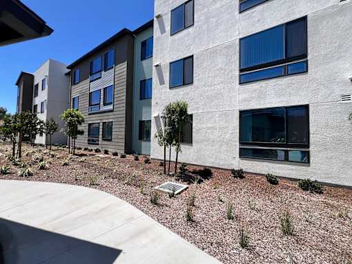 A modern building with a grey exterior and a landscaped area in front.