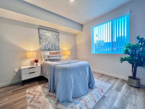A bedroom with a bed, nightstand, and a potted plant.