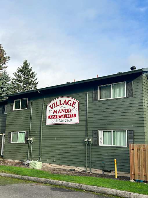 A green building with a sign that says Village Manor Apartments.