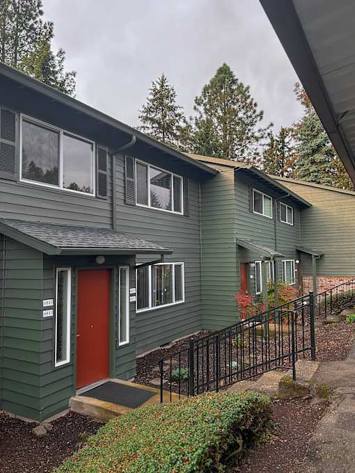 A green house with a red door and a black fence.