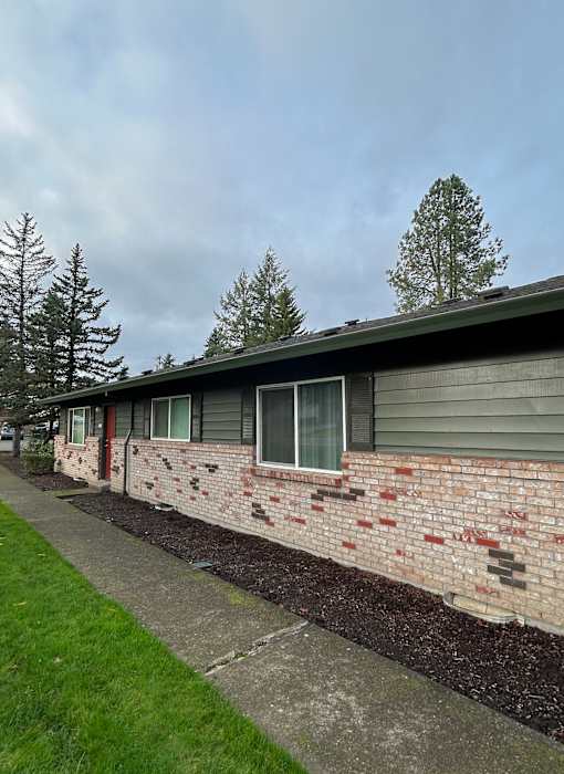 A building with a grey roof and a brick wall with a small garden in front.