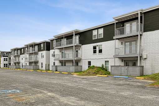 Apartment complex with grey and white buildings and a parking lot in front.
