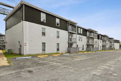 Apartment complex with grey and white buildings and a parking lot in front.