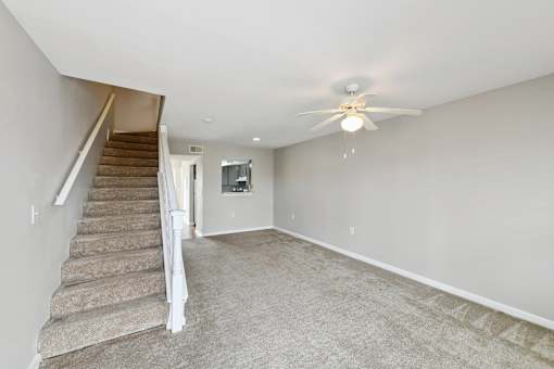 A spacious room with a staircase and a ceiling fan.