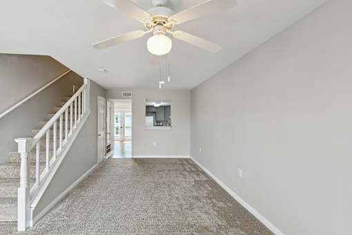 A spacious room with a carpeted floor and a ceiling fan.