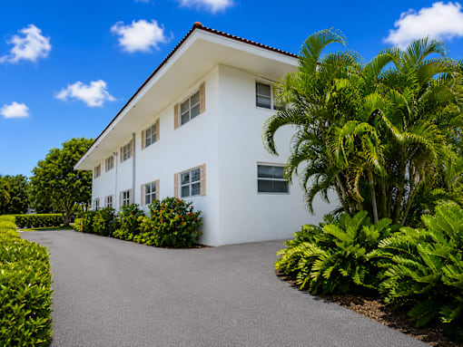 A white house with a driveway and green plants.