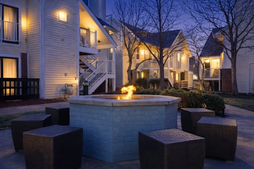 A fire pit in the middle of a courtyard surrounded by wicker chairs.