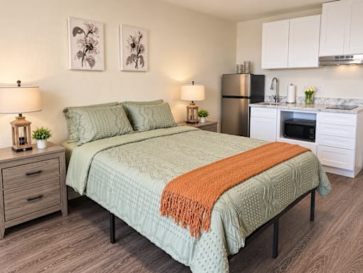 A bedroom with a bed, nightstands, and a kitchenette.
