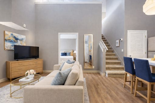 A living room with a beige couch, a coffee table, and a staircase.