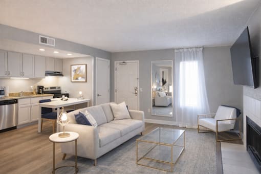 A living room with a white couch, a glass coffee table, and a flat screen TV mounted on the wall.