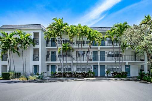 A large white building with balconies and palm trees in front.