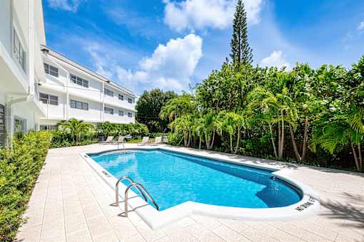 A swimming pool surrounded by trees and a white building.