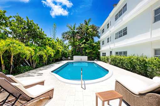 A pool surrounded by trees and chairs.