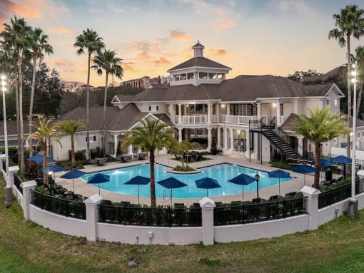 a clubhouse with a large pool and umbrellas at sunset