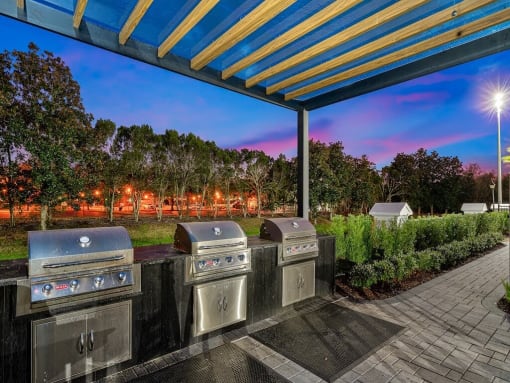 a group of stainless steel gas grills under a blue and yellow roof