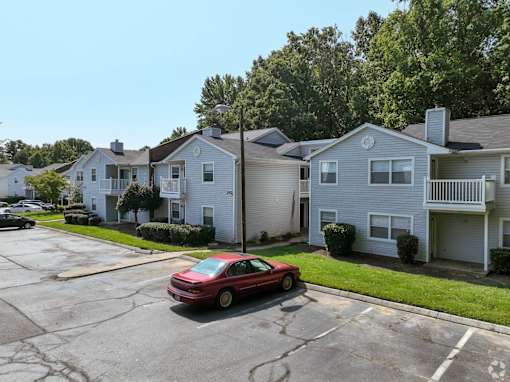 A red car is parked in a parking lot in front of a house at Sedgefield Square Apartments, North Carolina, 27407