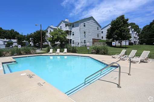 A swimming pool with a metal railing and lounge chairs in front of a large apartment building at Sedgefield Square Apartments, Greensboro