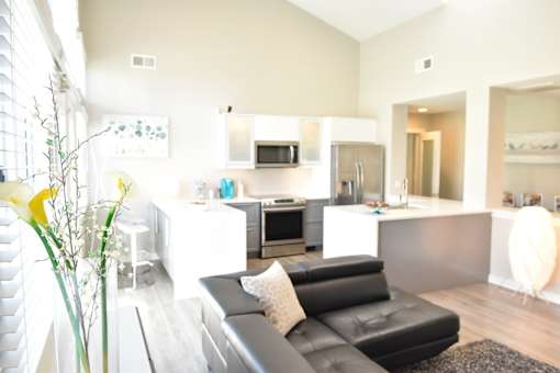 A black leather couch sits in a modern kitchen with white cabinets and appliances at Sedgefield Square Apartments, Greensboro, North Carolina