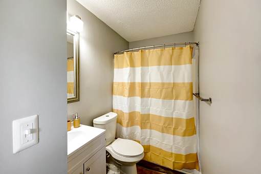 A bathroom with a toilet, sink, and striped shower curtain at Sedgefield Square Apartments, North Carolina, 27407