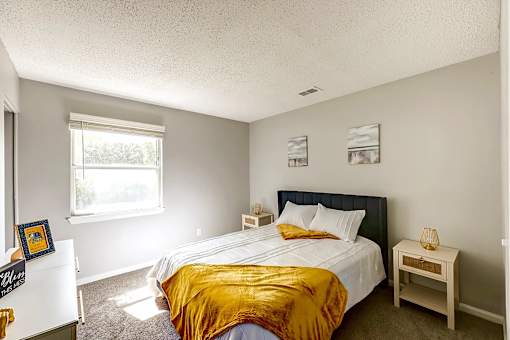 A bedroom with a bed, nightstand, and window at Sedgefield Square Apartments, Greensboro, NC, 27407