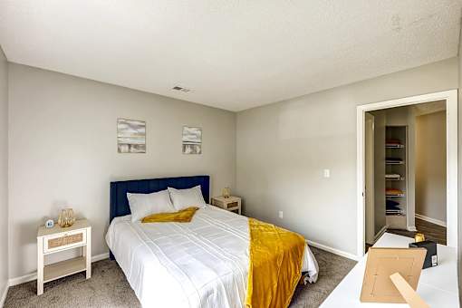 A bedroom with a bed, nightstand, and a yellow blanket at Sedgefield Square Apartments, North Carolina
