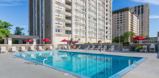 a swimming pool with chaise lounge chairs and umbrellas in front of a tall building at The Ivanhoe Apartments, Hackensack, NJ