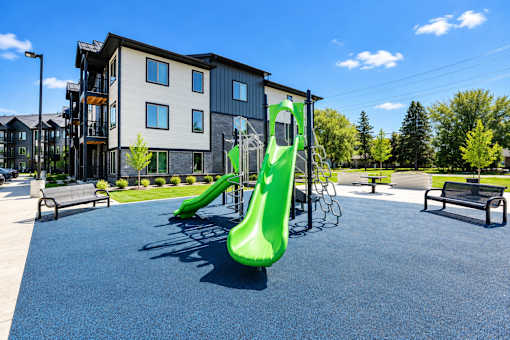 A playground with a green slide in front of a building.