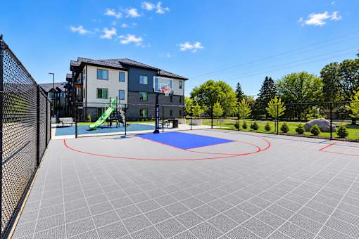 A playground area with a blue mat and red circles is surrounded by a fence and a building in the background.
