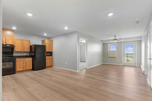 an empty living room with wood flooring and a kitchen