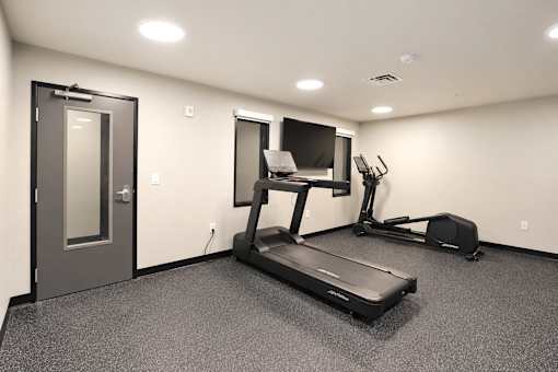 A room with a treadmill, exercise bike, and television.