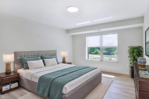 A bedroom with a large bed and a window overlooking a green area.