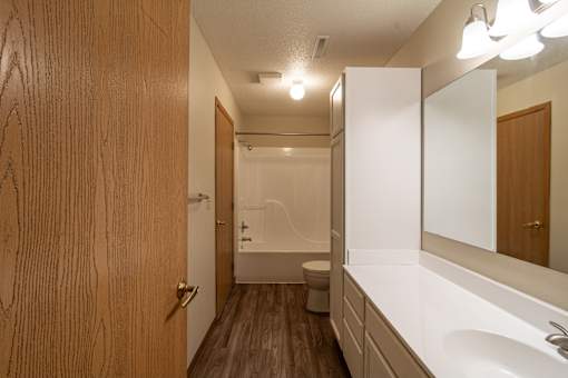 A small, clean, and well-lit bathroom with a wooden door and a white sink.