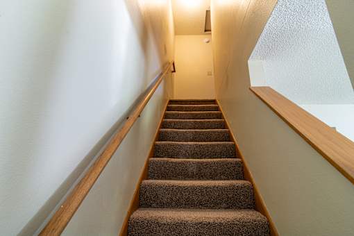A staircase with a brown carpeted runner and wooden handrails.