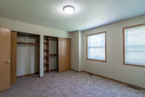 A room with a carpeted floor, a window with blinds, and a closet with shelves.