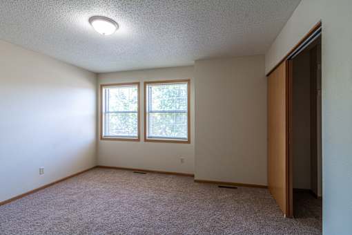 A room with a carpeted floor, a window with trees visible outside, and a closed door on the right.