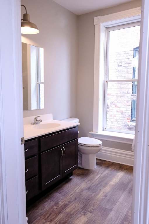 A bathroom with a toilet, sink, and wood flooring.