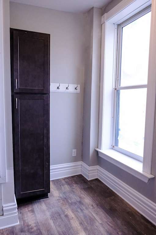 A tall dark brown cabinet stands in a room with a window.