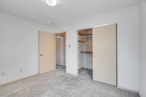 Secondary bedroom with wooden built-in inside closet and carpeted floor.