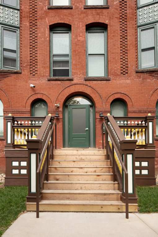 A red brick building with a green door and a wooden staircase.