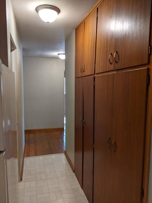 A hallway with a refrigerator on the left and wooden cabinets on the right.