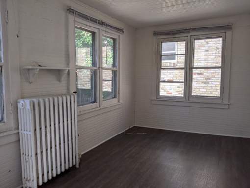 A white radiator sits in a room with wooden floors and two windows.