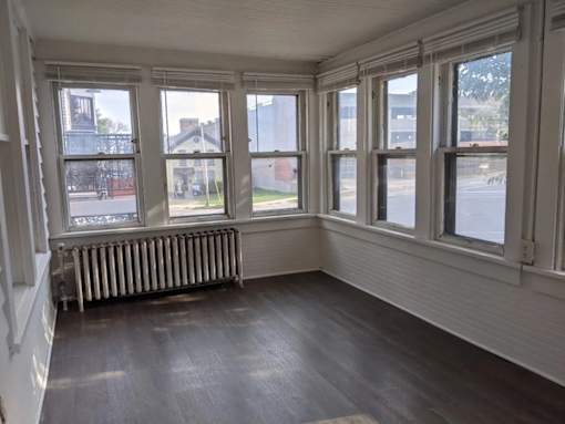 A room with white walls and a wooden floor with a window and a radiator.