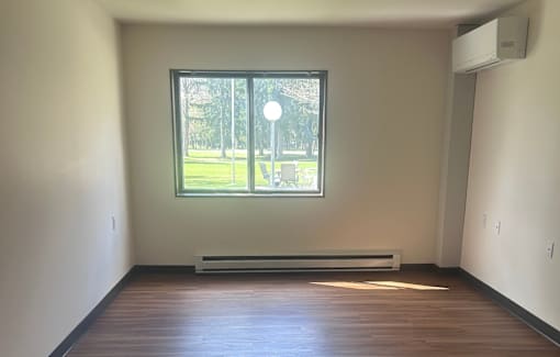 A room with a window overlooking a street with a white wall and a radiator.