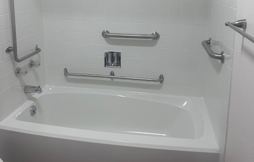 A white bathtub with silver grab bars on the wall.
